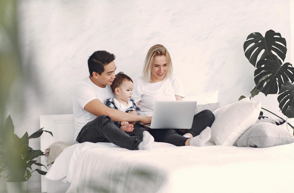 Image of a family of 3 sitting on a bed looking at a laptop PC